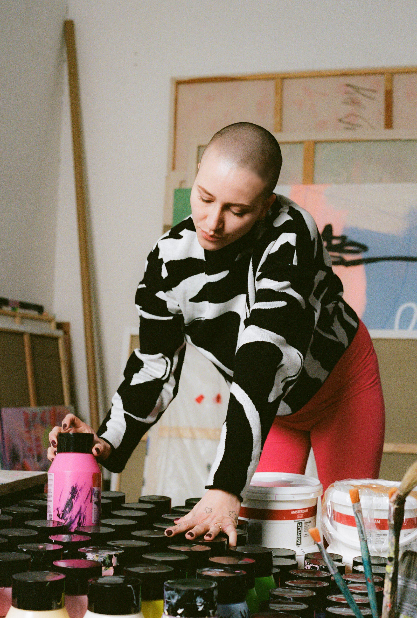 Fruzsina during painting prep Pregnant artist selecting paint supplies, dressed in MIUMI’s bright pink maternity pants.