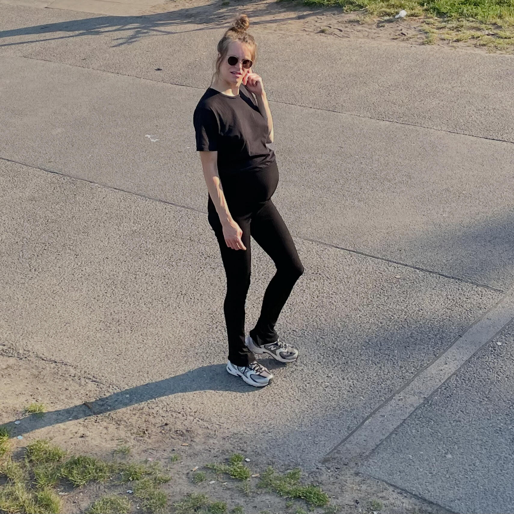Antonia, her head full of positive expectations Seen from above: Pregnant woman in black clothing walking on concrete on a sunny day.